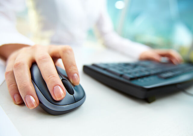 closeup of woman's hand clicking mouse and a keyboard in the background