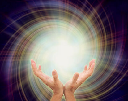 human hands appear to be holding a bright white ball of light with a multi colored spiral behind it