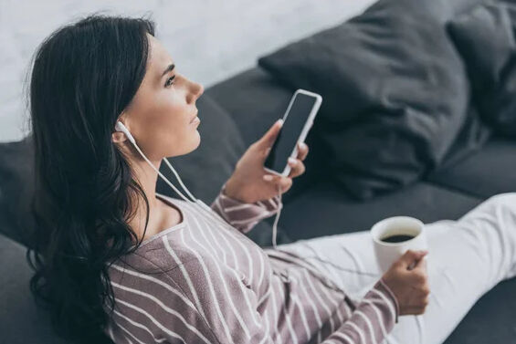 Woman Listening to Podcast with Headphones and Phone on a Couch with Coffee