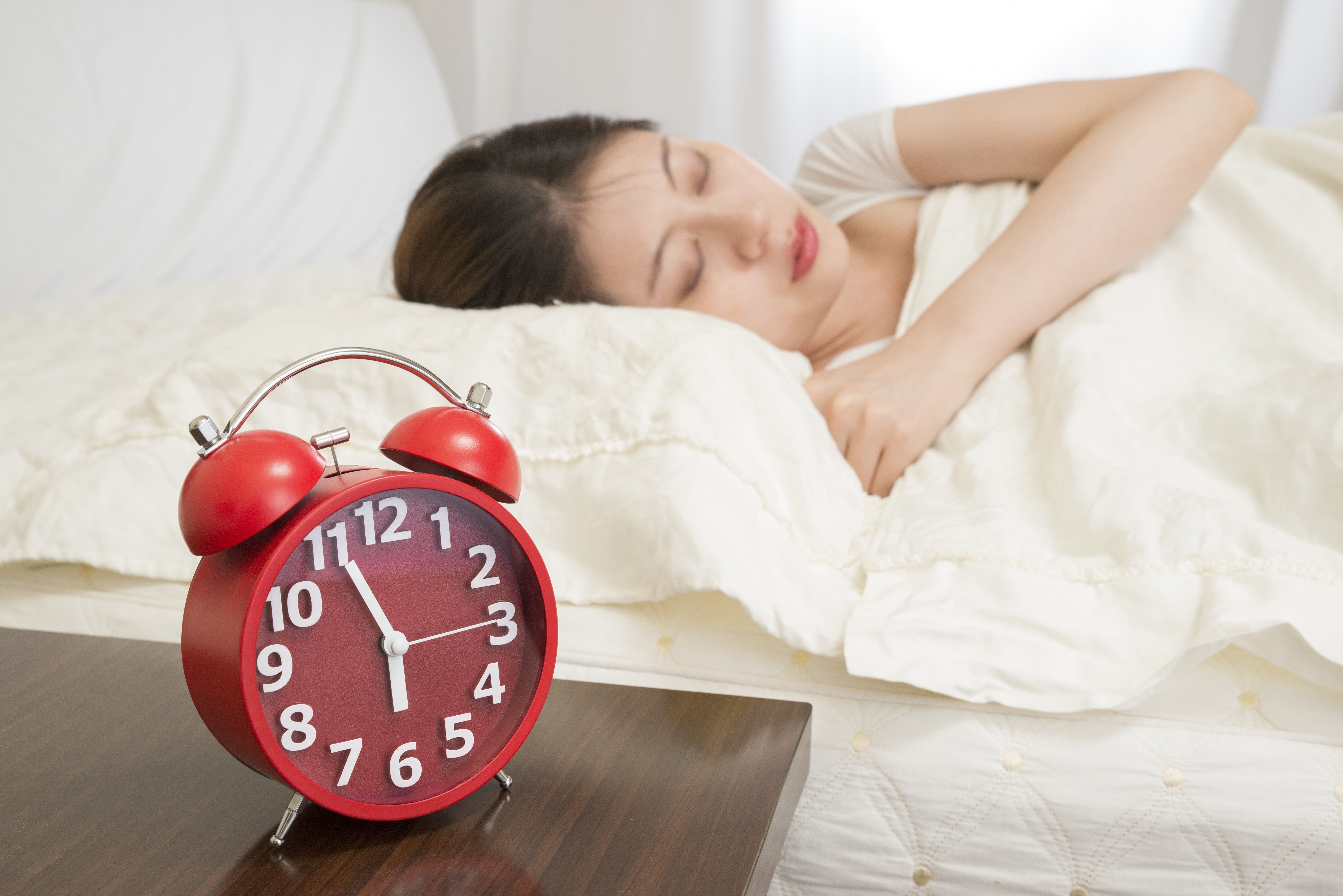young lady sleeping in bed with a red alarm clock