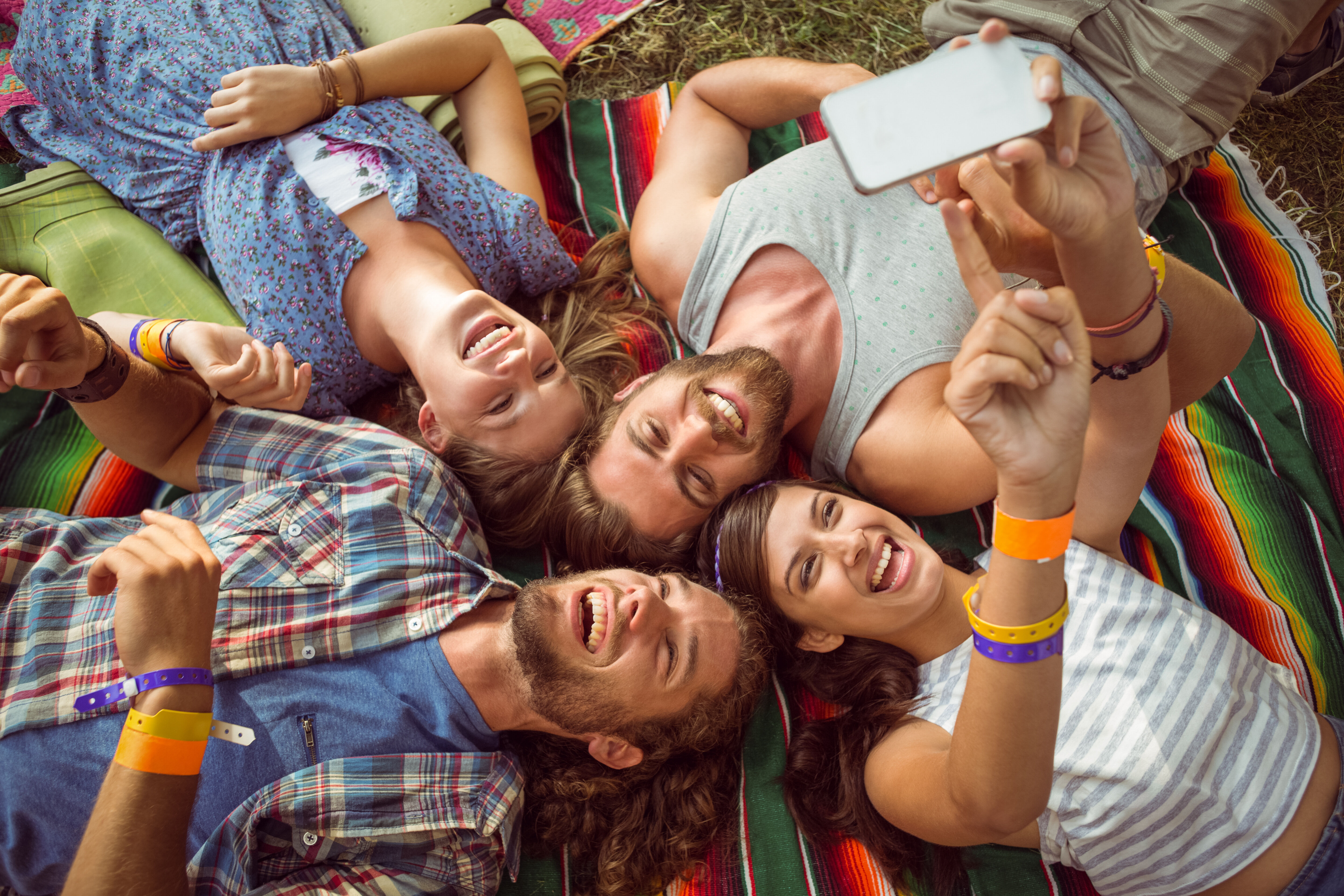 user generated content - arial shot of 4 friends laying on a brightly colored blanket wearing wristbands and taking a selfie