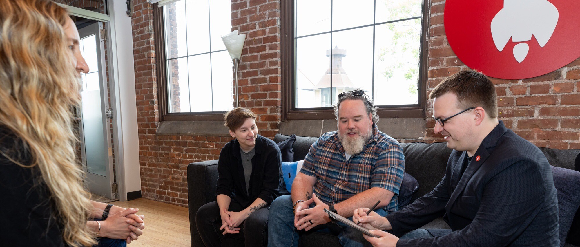 Four people engaged in a discussion while sitting on a couch in a modern office space.
