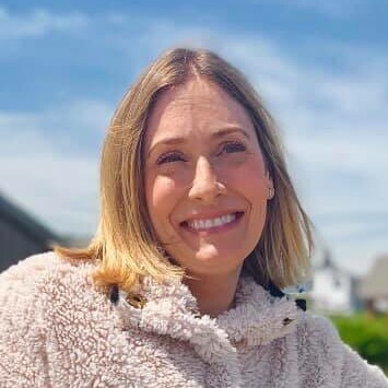 Smiling person in a cozy sweater against a blue sky.