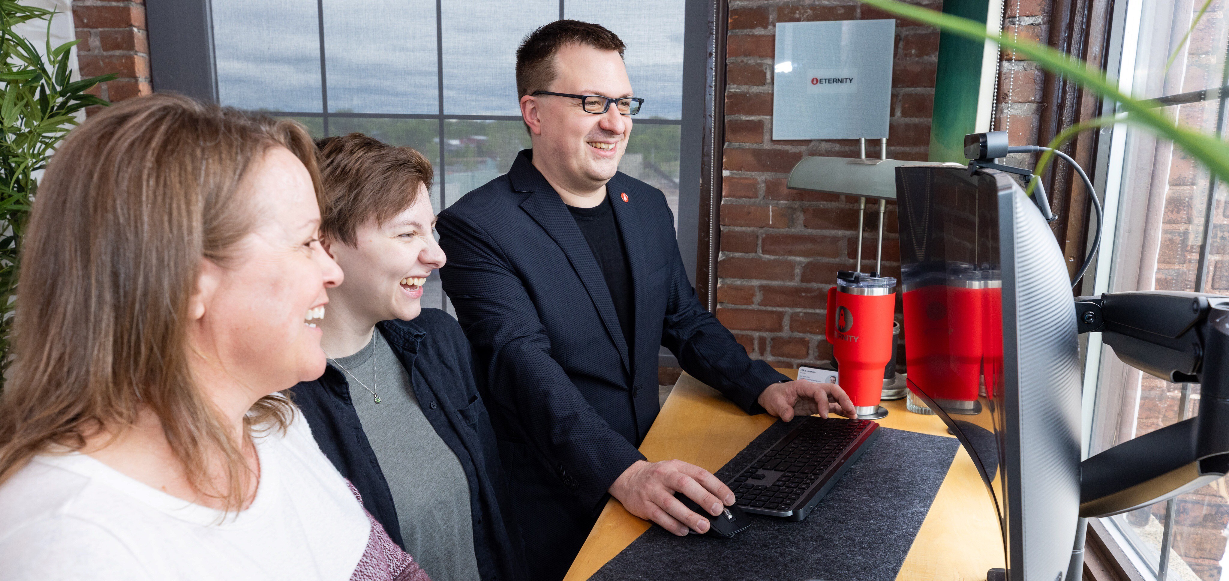 Three people smiling while working at a computer in a bright office setting
