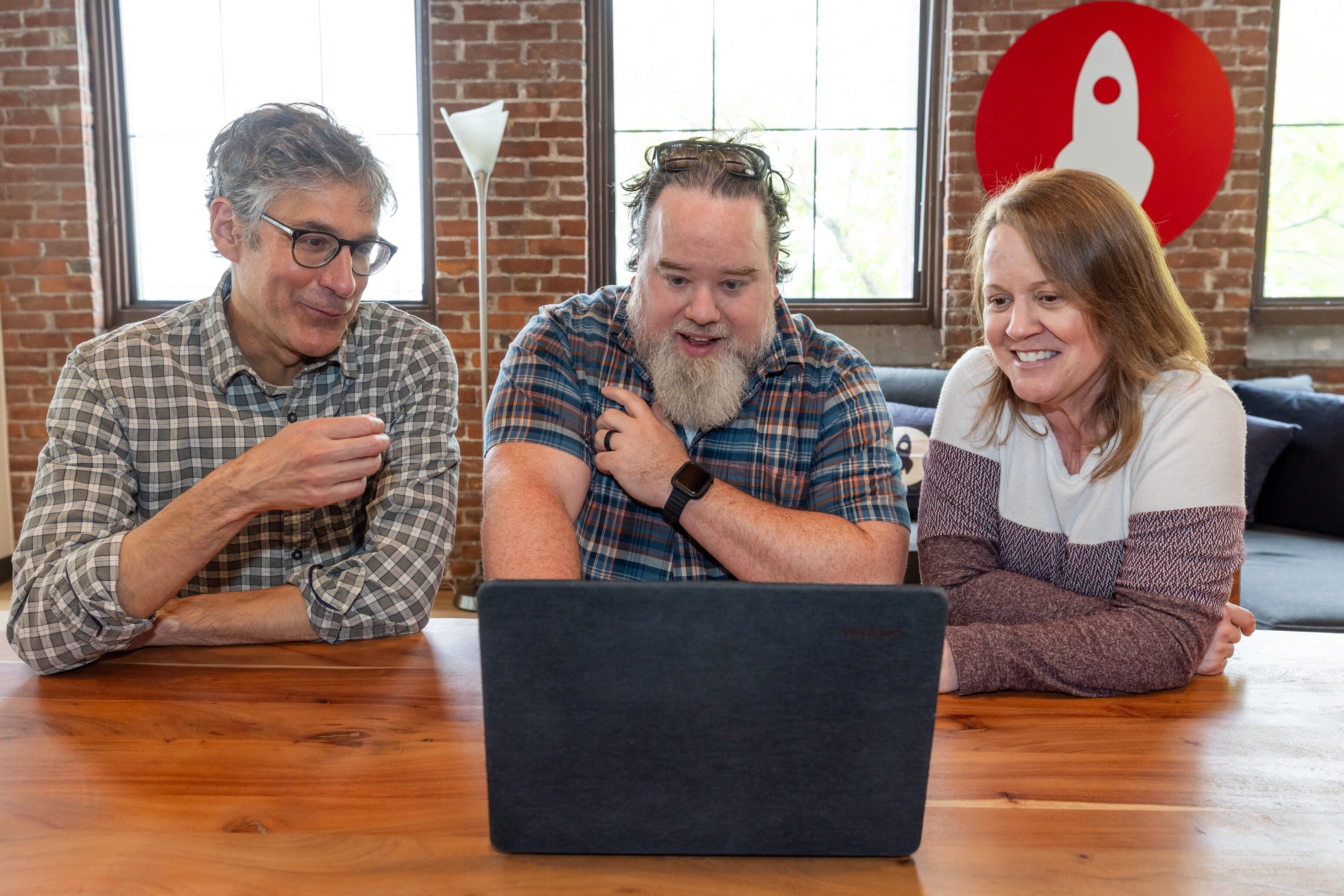 Three people gathered around a laptop, smiling and engaging with the screen.