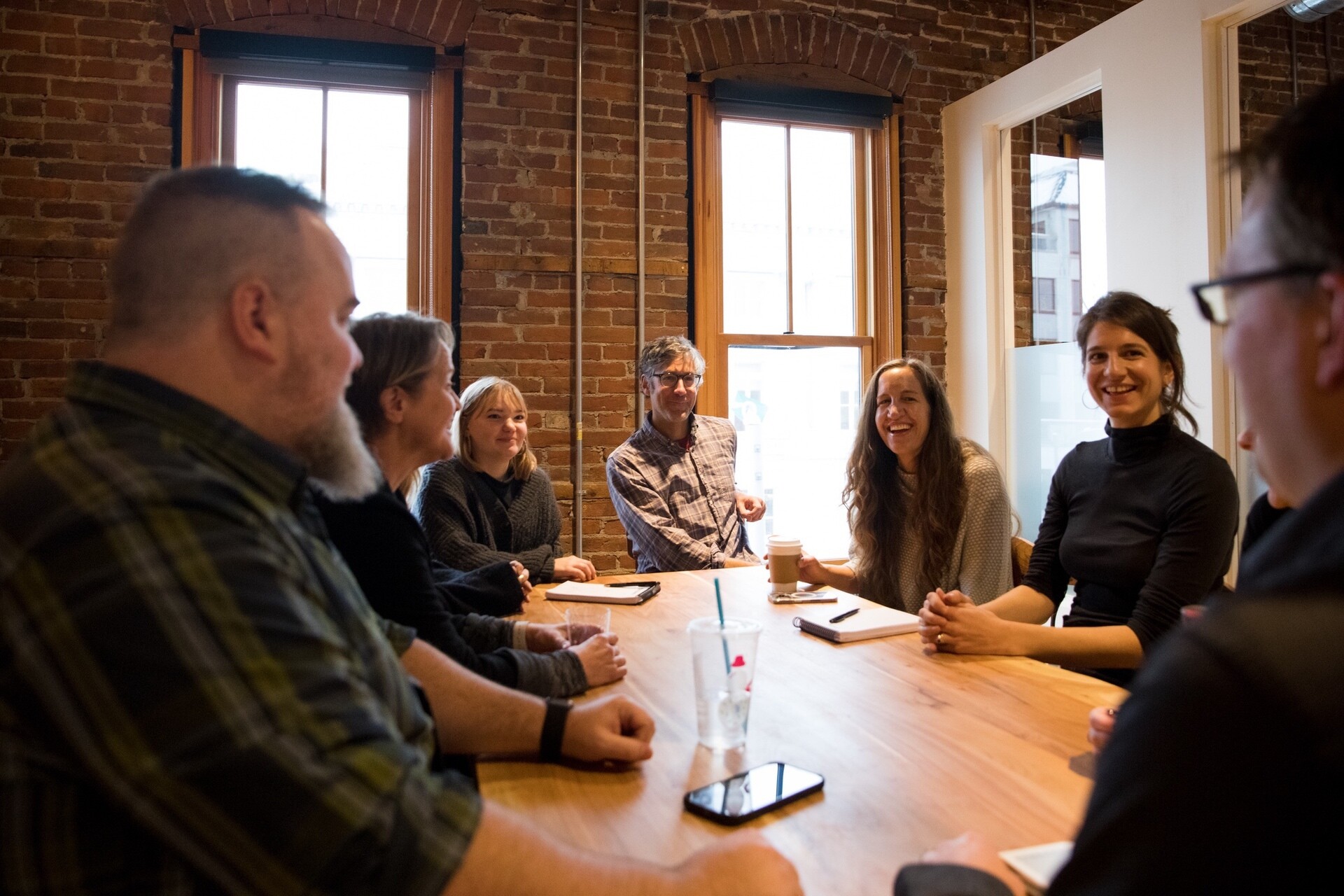 A group of eight people engage in a meeting around a wooden table in a cozy room.