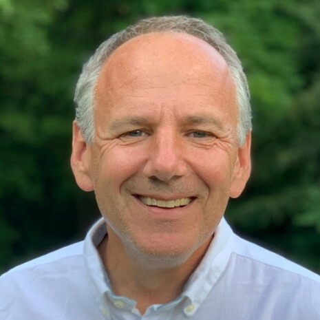 Smiling man in a light shirt against a green, natural background.