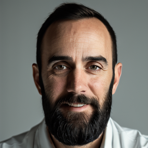 Close-up portrait of a man with a beard, smiling against a neutral background.