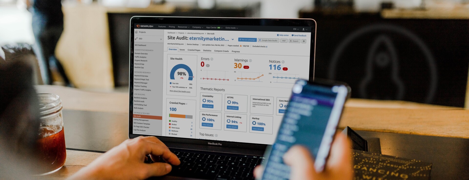 Person using a laptop with an SEO site audit dashboard and a smartphone on a table