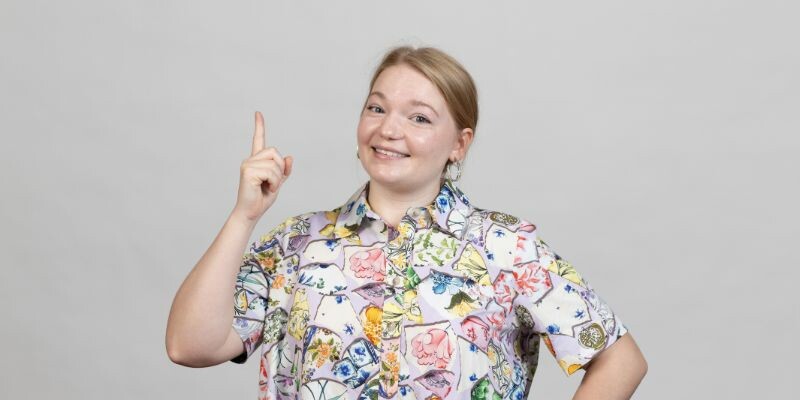 Kalei Harris, Eternity web designer, smiling and pointing upward against a gray background.