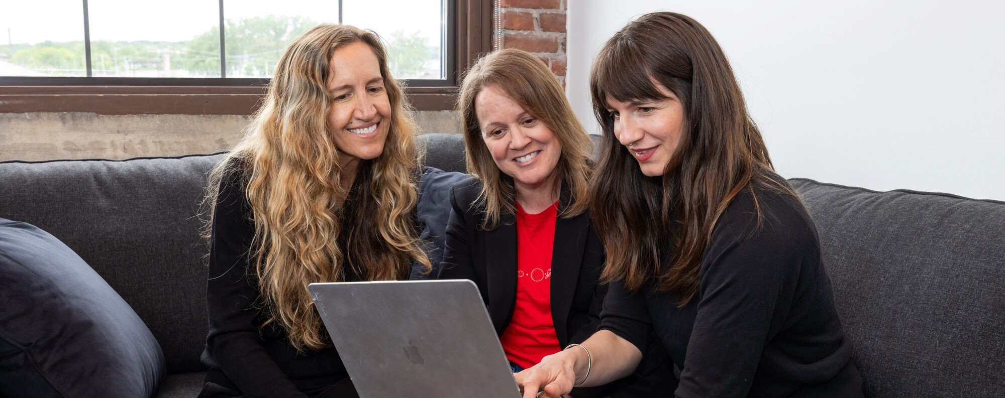 Three women working together on a laptop while sitting on a couch.