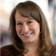 Smiling woman with long brown hair in a softly blurred background.