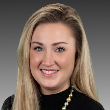 Smiling woman with long blonde hair wearing a black top and pearl necklace.