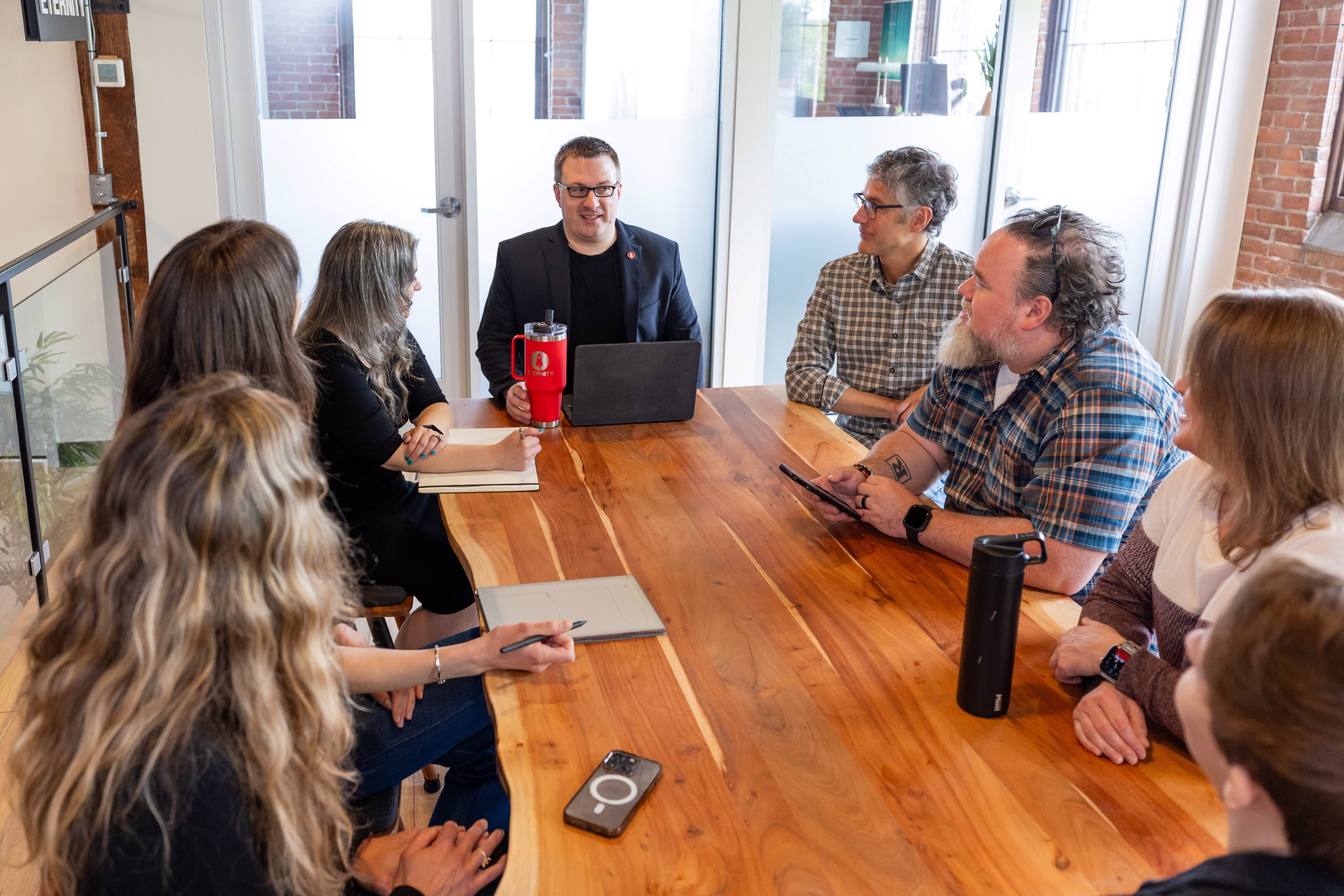 A group meeting around a wooden table with a speaker presenting at a laptop.