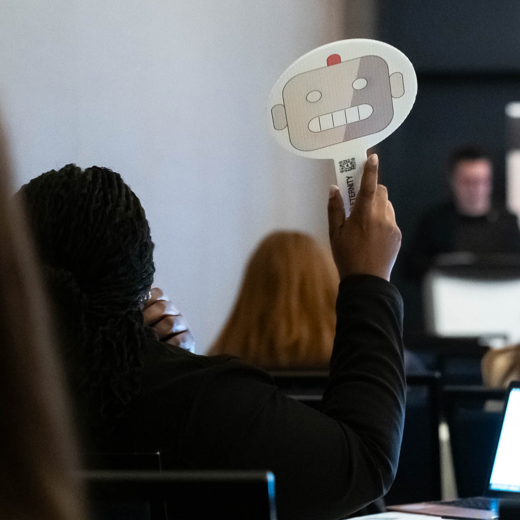 A participant holds up a robot-themed sign during a conference presentation.
