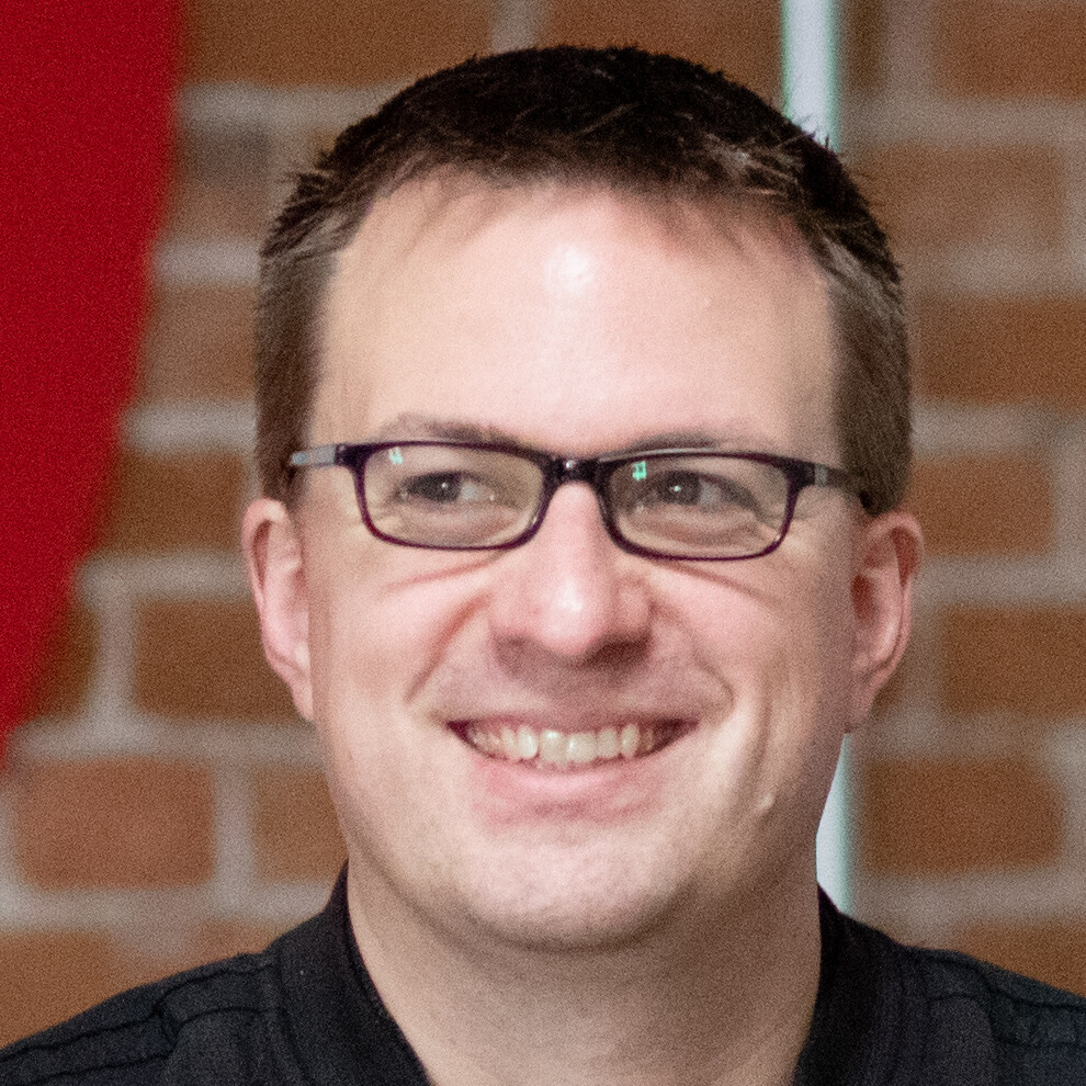 Smiling person with glasses against a brick background.