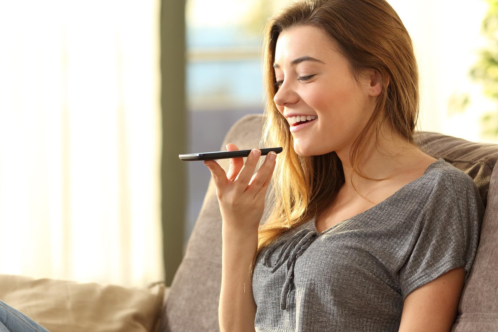 A woman sitting on a couch using voice commands on her smartphone