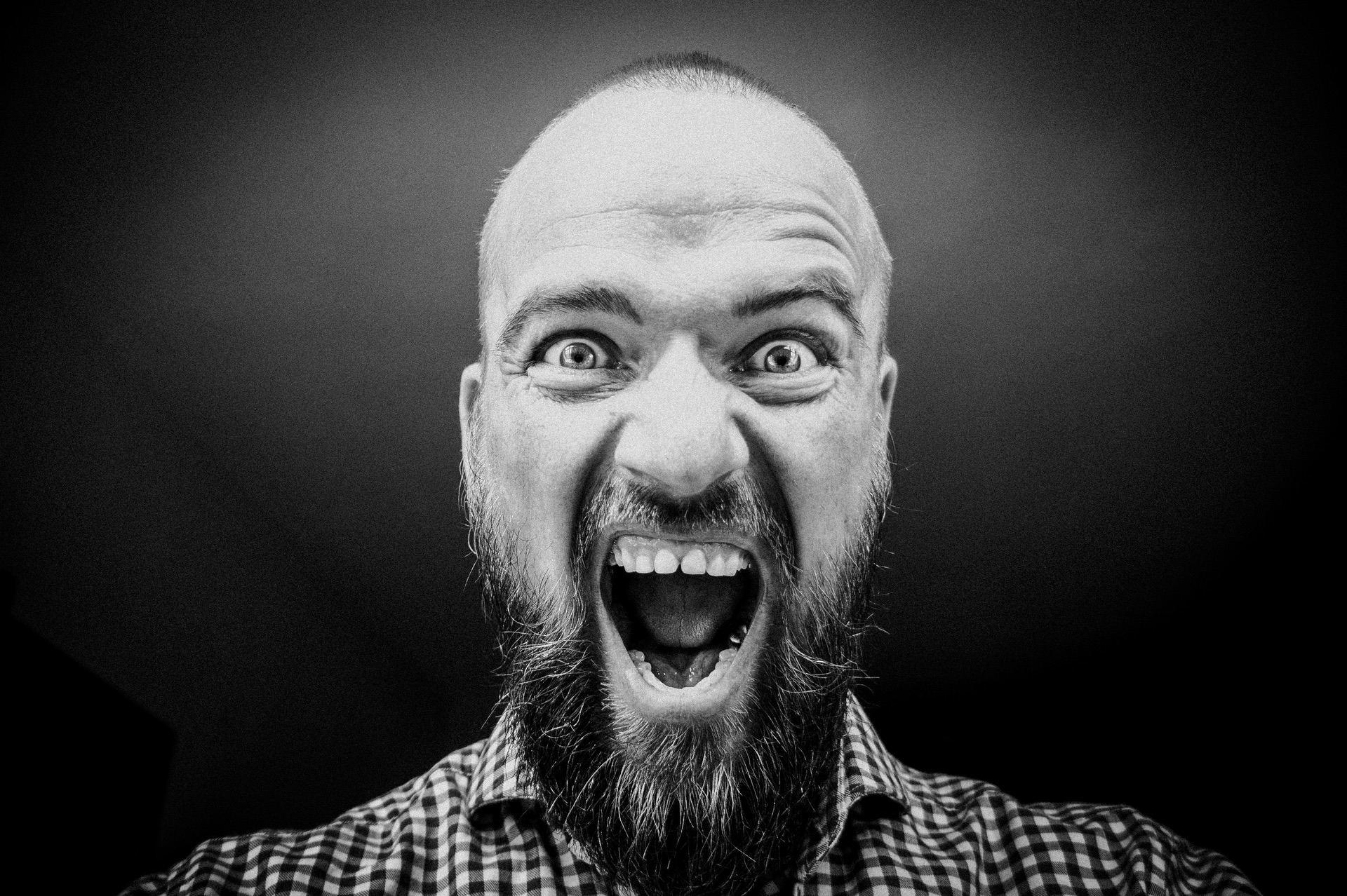 Man with a beard screaming intensely in black and white image