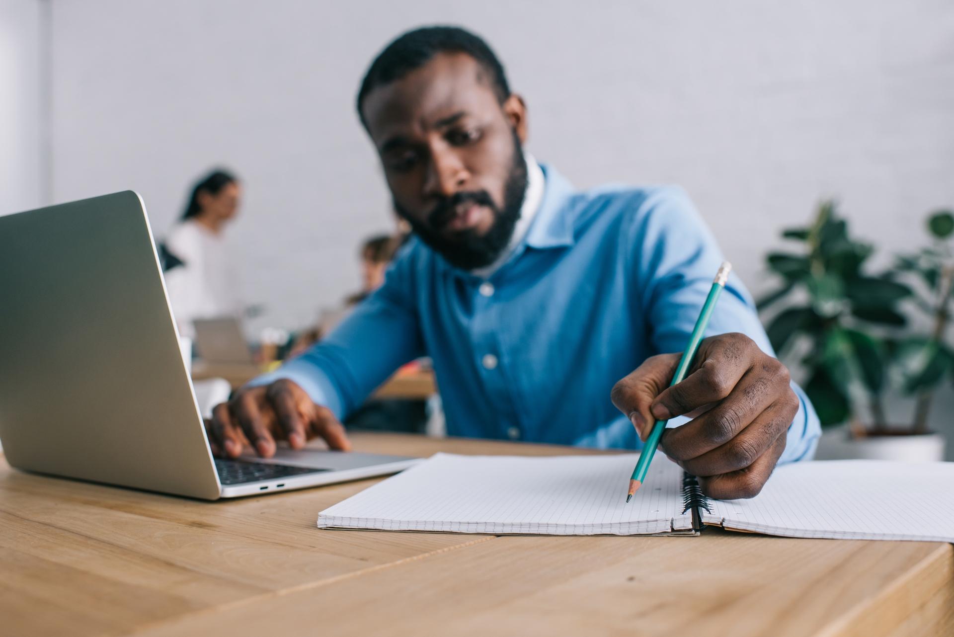 Black man sitting at laptop writing notes
