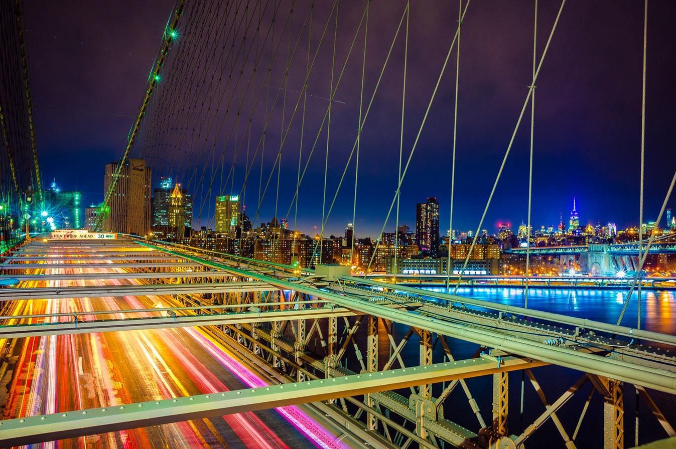 Night view of a city skyline with lights and a busy bridge in the foreground