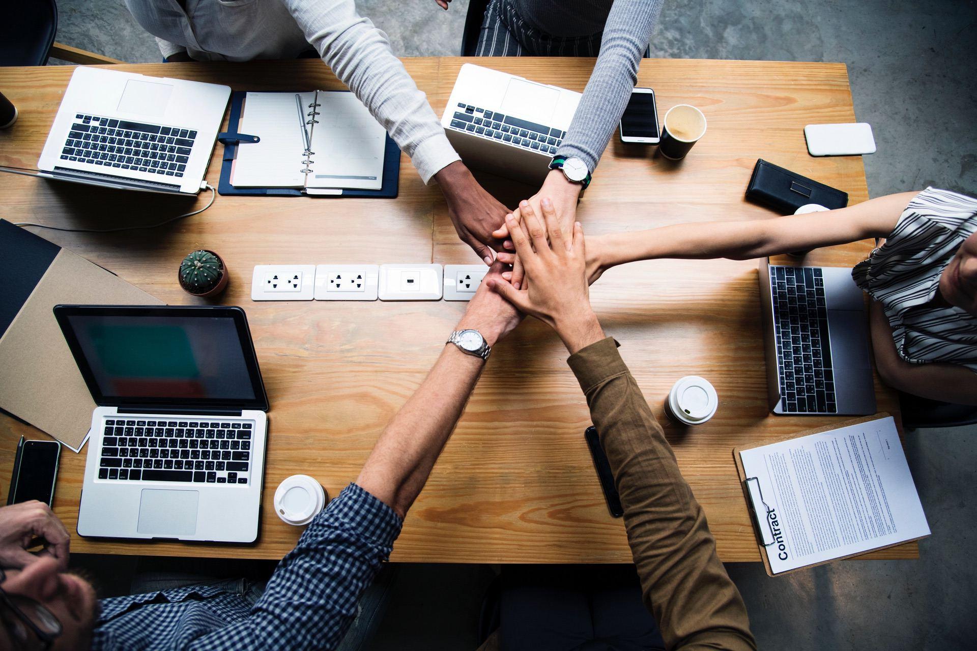 Hands joining together on a table with laptops and documents present