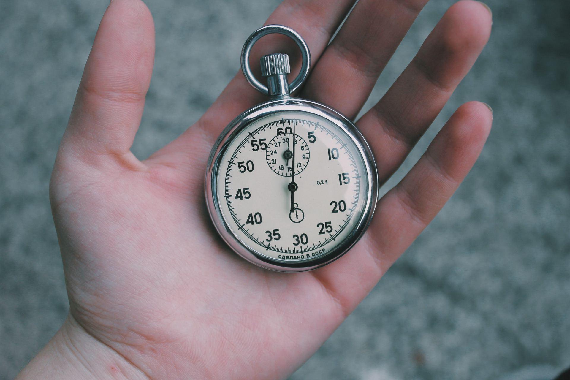 A hand holding a vintage stopwatch with a white dial and black numbers