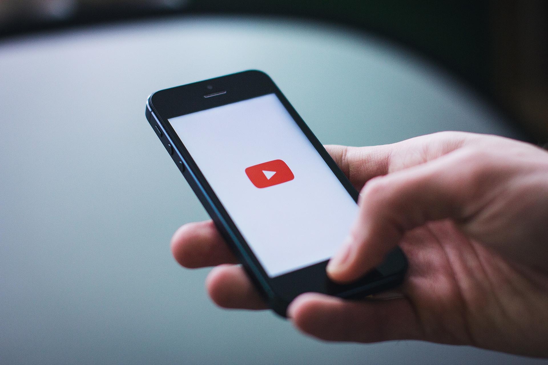 A hand holding a smartphone displaying the YouTube logo on the screen