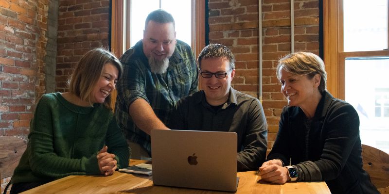 Eternity collaboration with a client in action: 4 people share ideas while looking at a laptop in a rustic office setting.