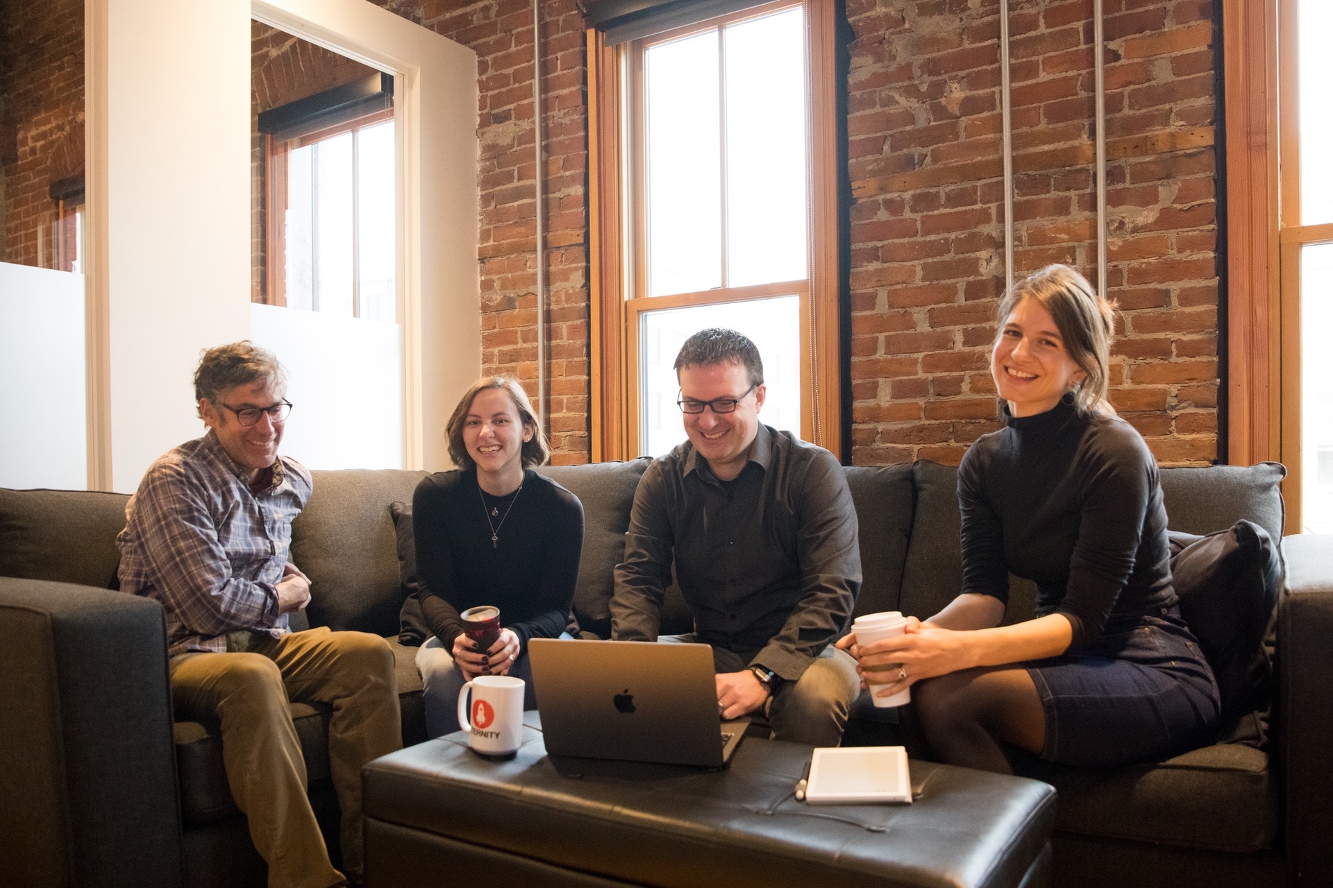 Group of four people seated on a couch with a laptop and drinks in a cozy setting