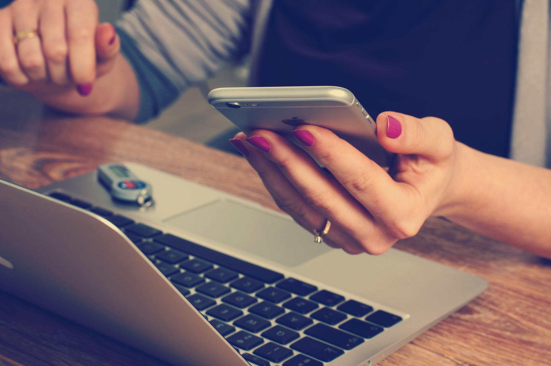 Hand holding a cell phone over a laptop