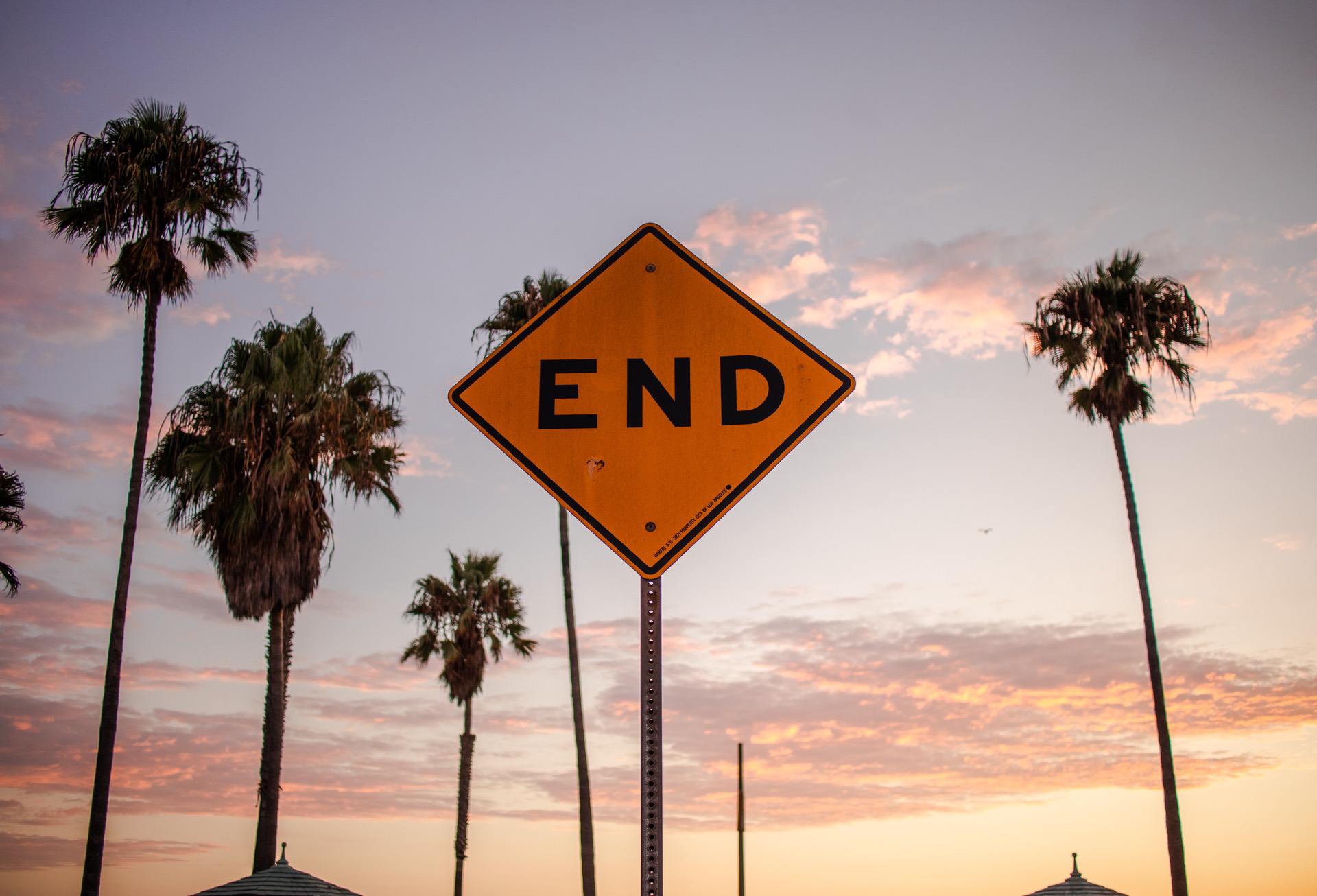 A yellow "END" road sign with palm trees against a sunset sky