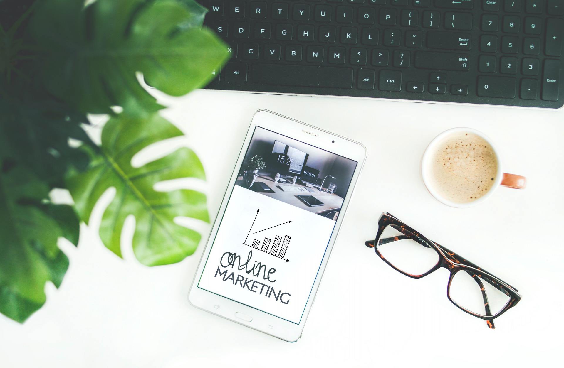 Tablet displaying online marketing graphic, glasses, coffee, and plant on desk
