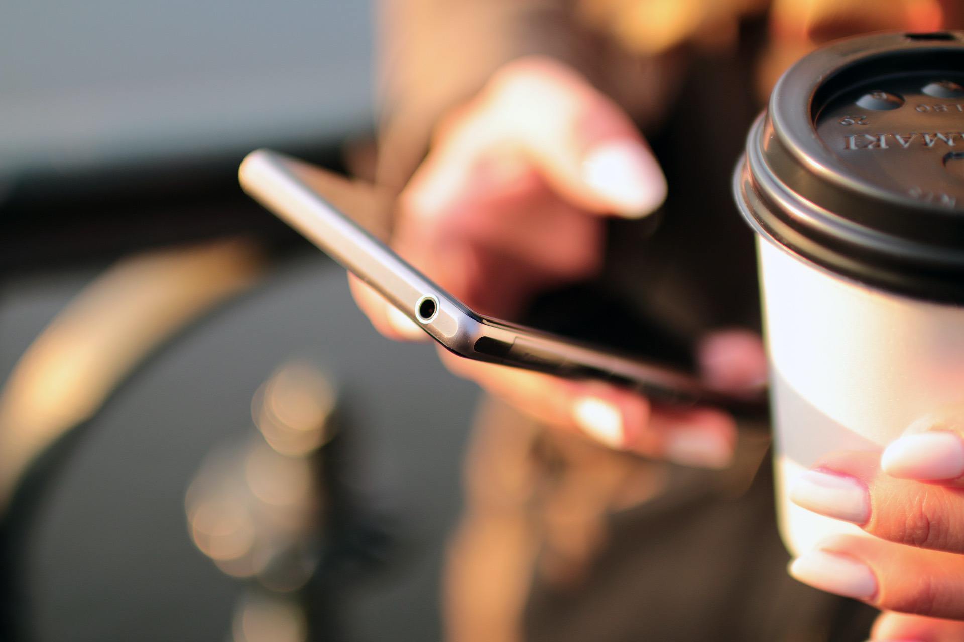 A person holding a smartphone and a coffee cup outdoors