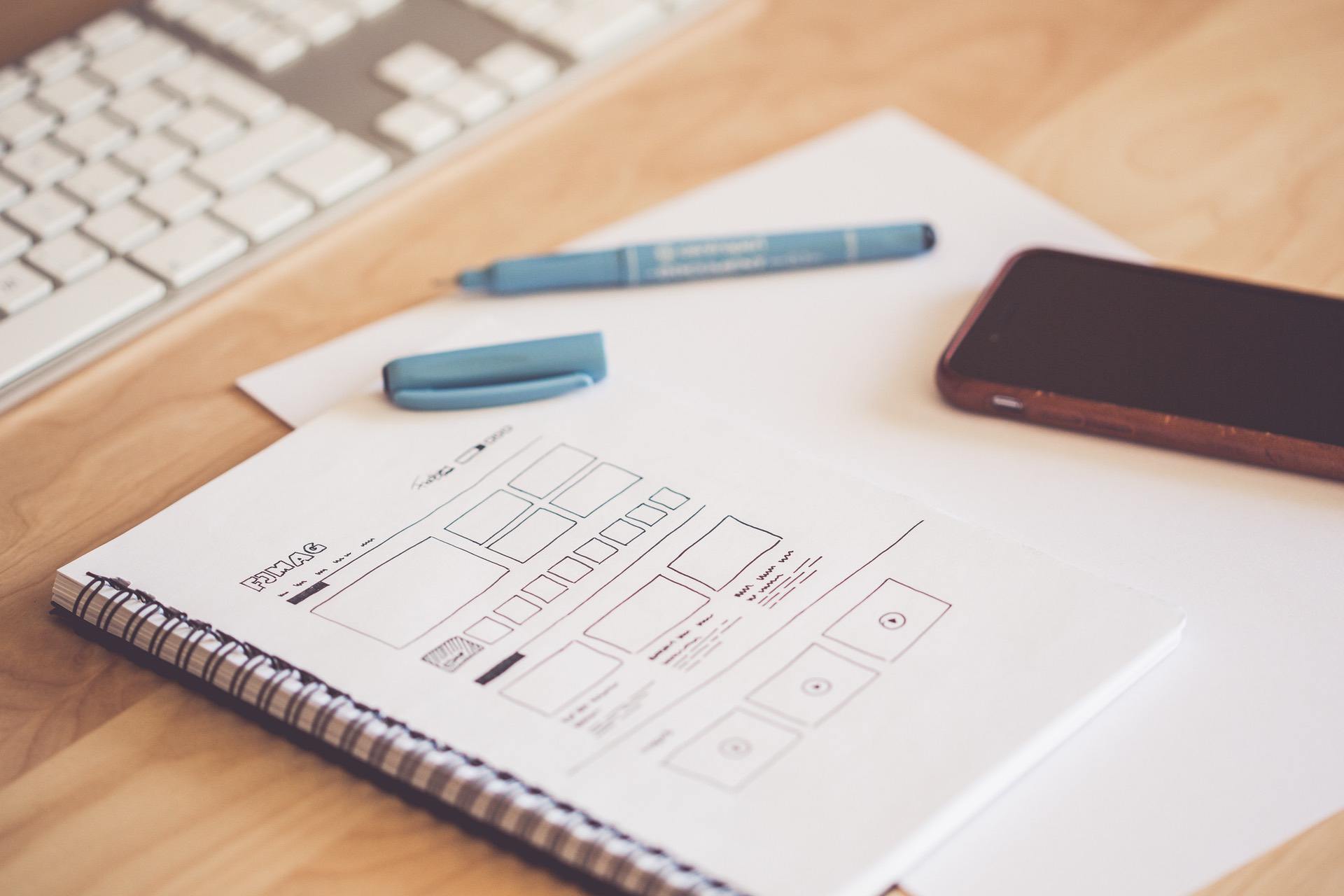 Spiral notebook with layout sketches, marked pen, paper, and a smartphone on a desk